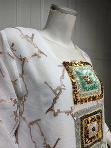 Macro detail of multicolored sequins and gold branch embroidery on white cotton fabric
