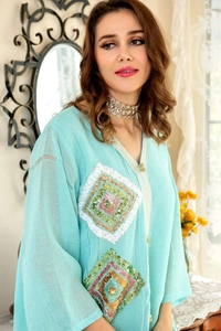 Détail de robe turquoise en lin avec broderie de paillettes colorées et bordure dorée