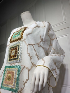 Detail of white long sleeve dress with sequin embroidery and gold leaf texture patterns