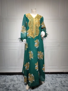 Détail d'une robe maxi vert foncé avec broderie dorée et finitions en plumes