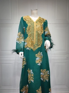 Détail de la robe vert foncé avec broderie dorée et finitions plumes aux manches