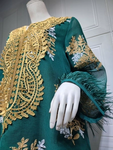 Détail d'une robe vert foncé avec broderie dorée et plumes aux poignets des manches