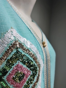 Détail d'une robe vert menthe avec des paillettes colorées et une bordure dorée tissée