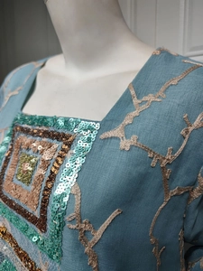 Macro detail of teal linen dress featuring square sequins embroidery and floral branch patterns