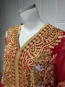 Détail de la broderie dorée complexe et des motifs floraux blancs sur la robe rouge