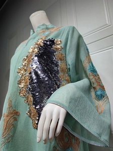 Detailansicht eines eleganten grünen Abendkleides mit gold-schwarzer Paillettenstickerei.