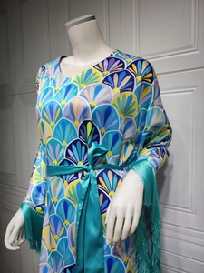 Détail de la robe en satin avec motifs géométriques et pompons turquoise aux poignets
