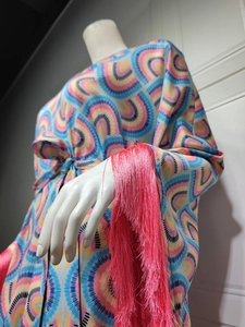 Close-up of vibrant geometric print dress featuring long pink tassels on wide sleeves