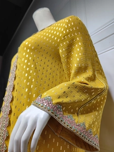 Detail der Goldfolienprägung und bunten Paillettenspitze auf dem senfgelben Kleid