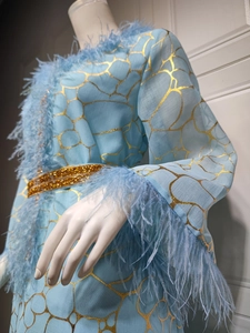 Details eines hellblauen Kleides mit goldenem Rissmuster und edlem Federbesatz am Saum