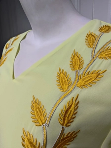 Detailed view of leaf embroidery with gold and silver threads on a V-neck dress