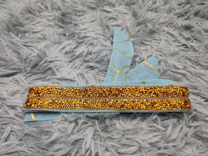 Detail eines hellblauen Kleiderstoffs mit Goldfolienstruktur und feinen Perlenstickereien