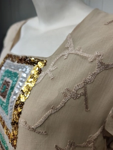 Detailed embroidery with vibrant sequins and geometric patterns on an apricot dress