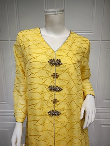 Detail of yellow kaftan showing intricate embroidery and ornate gemstone buttons on the V-neck