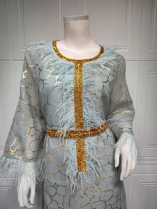 Detail eines hellblauen Kaftankleids mit Goldmustern und Straußenfederbesatz