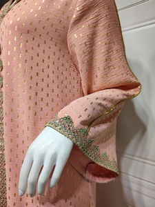 Detail des orange-rosa Kleides mit Goldfolienmustern und grün gestickten Spitzenmanschetten