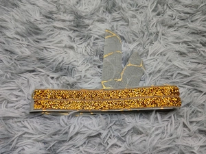 Nahaufnahme von grauem Stirnband mit goldenem Rissmuster und funkelnden Strasssteinen