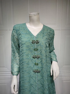 Detail of green mesh dress featuring V-neck silver trim and gemstone button closures