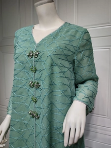 Detail of green mesh dress featuring intricate geometric embroidery and rhinestone flower buttons
