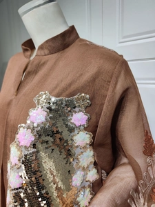 Detailaufnahme von schimmernden Gold- und Rosa-Pailletten auf einem braunen Abendkleid