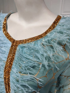 Detail eines hellblauen Kleides mit V-Ausschnitt, Golddruck, Strass und Straußenfedern