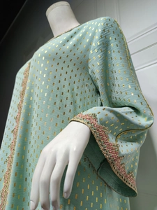 Detailaufnahme von Goldfoliendruck und feiner Stickerei auf dem minzgrünen Kleid