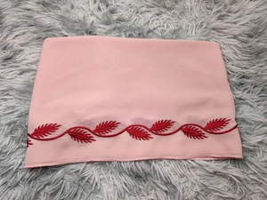 Detailed embroidery of red leaves on pink chiffon hijab fabric over a grey plush rug