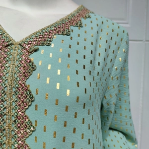 Detail von mintgrünem V-Ausschnitt mit Spitze, Goldpailletten und Folienrechteckmustern
