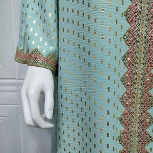 Detail eines minzgrünen Kleides mit Goldfolienmustern und Pailletten-Spitzenbesatz am Ärmel