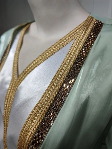 Detail of mint green satin caftan with gold embroidery and amber gemstone accents