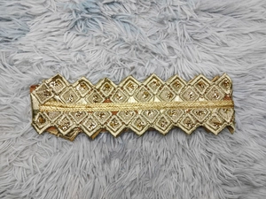 Close-up of golden geometric sequin embroidery and woven belt detail on chiffon dress
