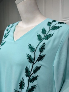 Detail of green leaf embroidery with silver silk threads on light blue chiffon dress