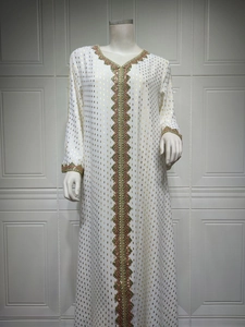 Detailansicht der Goldfolientextur und Stickerei an einem weißen Kaftan mit V-Ausschnitt