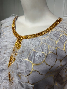 Detail eines grauen Kaftans mit Goldpailletten, Metalldruck und elegantem Federbesatz