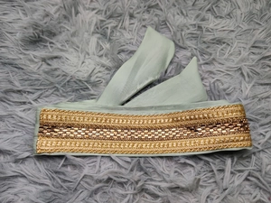 Detailed close-up of luxurious pale green silk belt with gold geometric embroidery