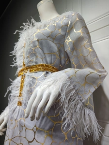 Detail eines hellblauen Kaftan-Kleids mit Goldfoliendruck und weißem Federbesatz