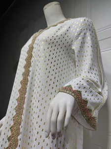 Detail von weißem Kleid mit Goldfolienmuster und buntem Pailletten-Stick am Ärmelrand