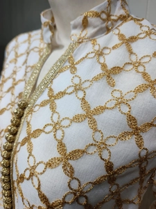 Dettaglio di ricamo floreale dorato e perline su scollatura di abito bianco