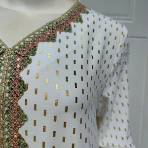 Detail eines weißen Kaftan-Ausschnitts mit bunten Pailletten und Goldfolienmustern