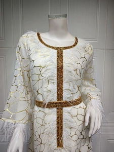 Detail eines weißen Langarmkleides mit goldenen abstrakten Mustern und Federbesatz-Akzenten