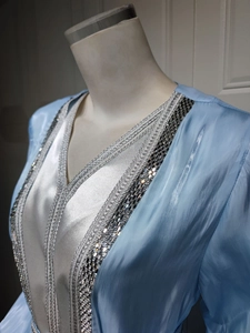 Macro detail of silver embroidery and rhinestone trim on light blue satin dress