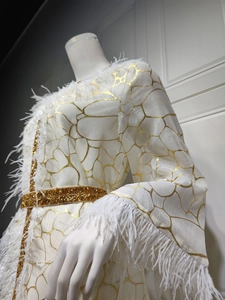 Details des weißen Abendkleides mit goldenen Rissmustern und Plüsch-Federbesatz