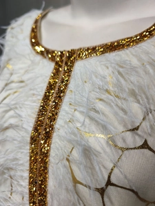 Detailansicht eines weißen Kleides mit goldenen Pailletten und Federbesatz-Applikationen