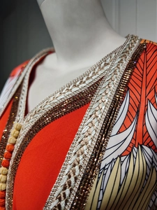 Detail of V-neckline with gold woven border and beaded crystals on orange kaftan dress
