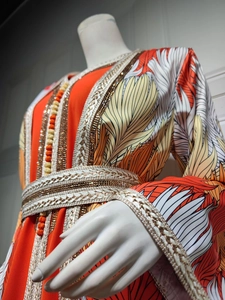 Detail of orange and white long dress with intricate beadwork embroidery and woven belt