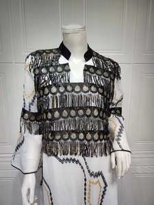 Detail of white evening dress with ethnic embroidery and gold sequin fringe accents