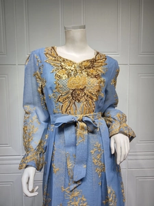 Macro detail of golden floral embroidery and sequins on light blue long sleeve kaftan dress