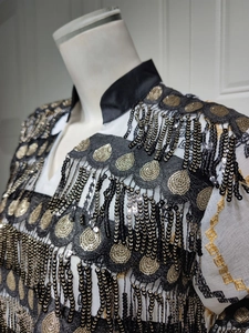 Detailed embroidery and black-gold sequin tassels on white evening gown upper section