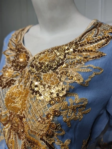 Close-up detail of golden sequin embroidery and floral patterns on light blue dress neckline