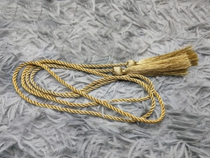 Dettaglio della cintura intrecciata dorata con nappe decorative su sfondo grigio